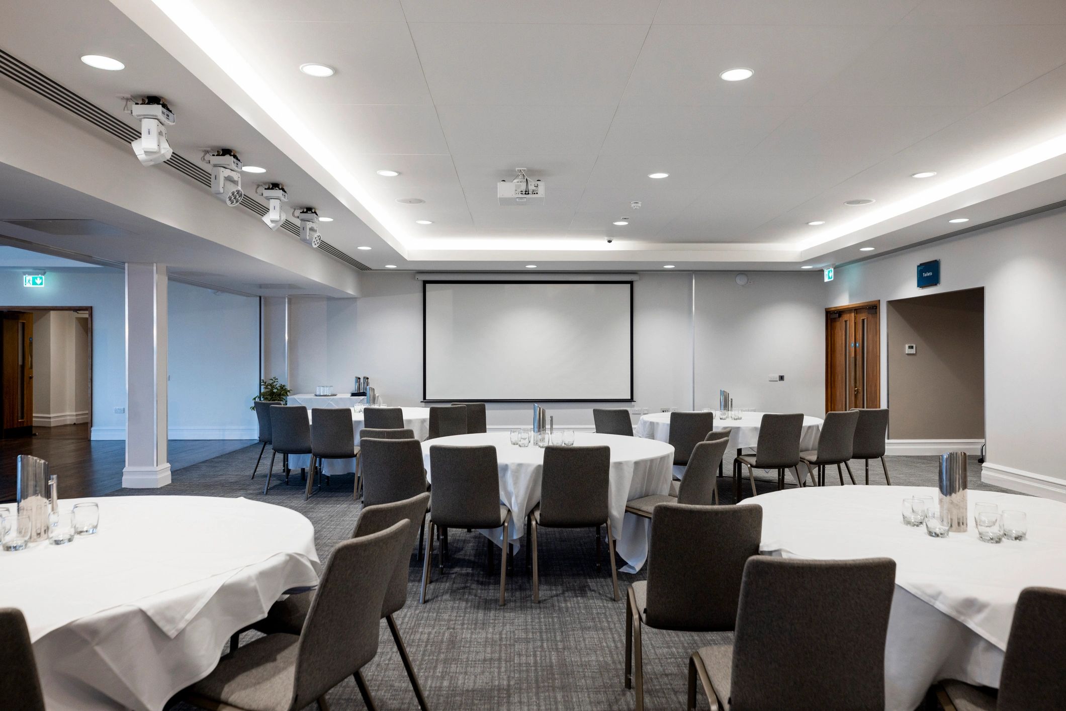 Wide view of a conference room with round tables and projector screen